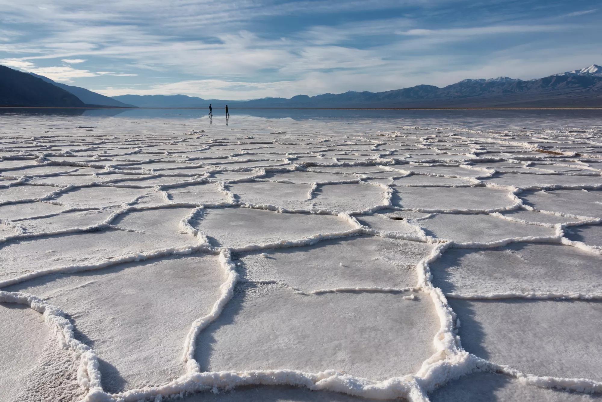 Two people in the disnce silhoutted at Badwater basin salt polygons in early morning light with mountains