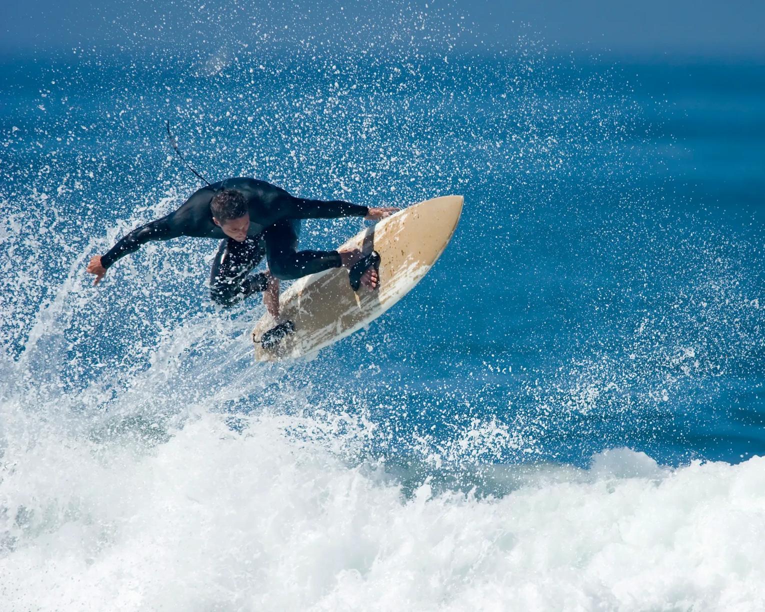 A man in a wetsuit surfing the waves on a pale yellow surfboard