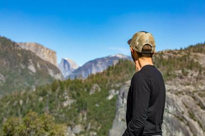 A man at overlook admiring Yosemite National Park in Ca, tall trees, towering mountains and flowing waterfalls. View of El Capitan and Half Dome. Spring 12:45am