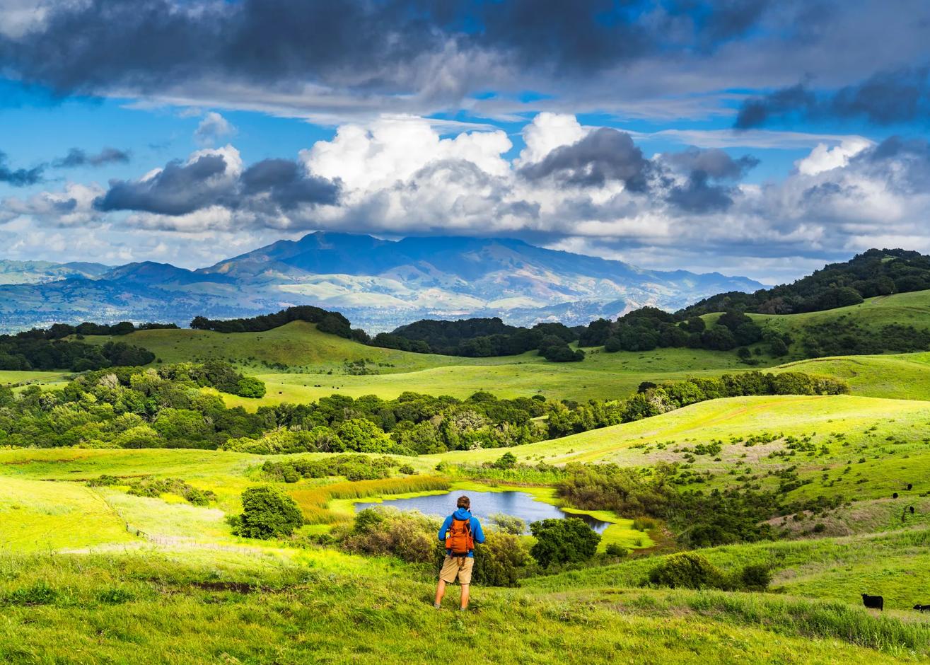 Hiker strolling through the lush green landscapes looking out at Mt. Diablo on a cloudy yet bright day in California.