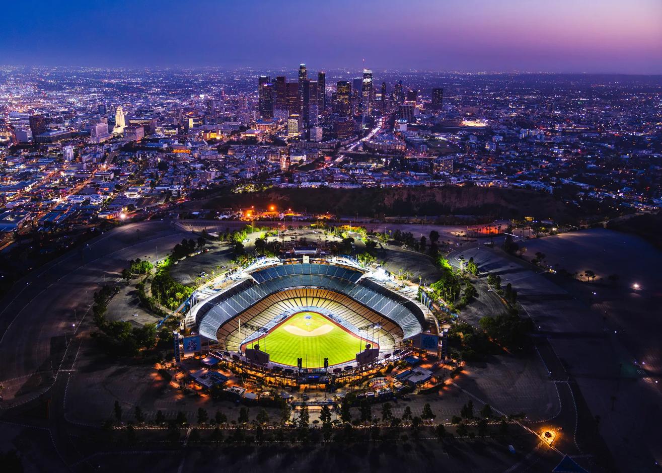 Aerial view of the Los Angeles skyline at night capturing the city lights of downtown high rises and an illuminated Dodger Stadium.