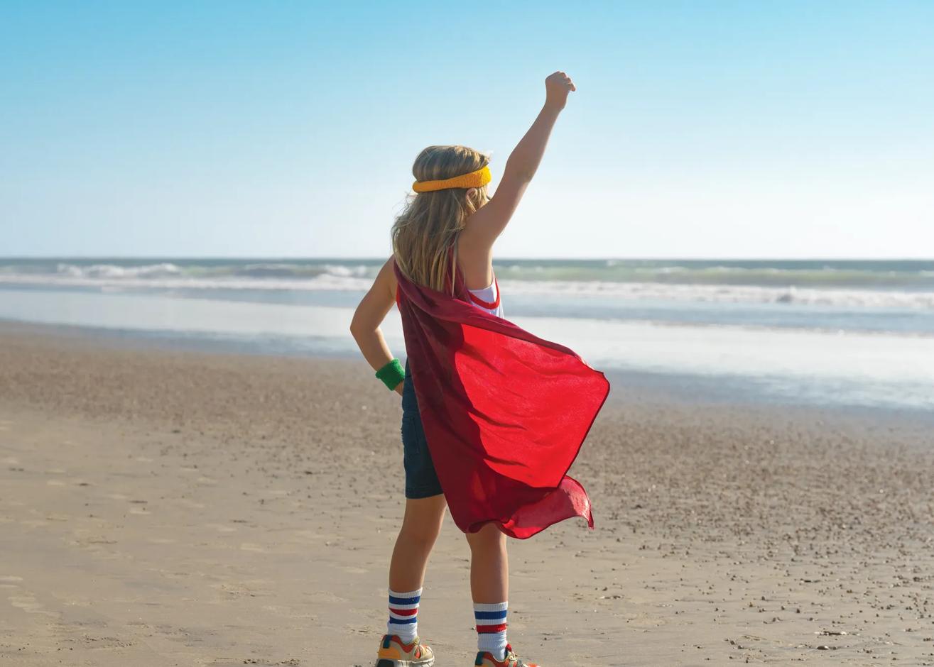 Kid standing on the beach in a power stance with a cape on, a scene from the "Childhood Rules" spot as part of the "Kidifornia" campaign photography captured during the commercial filiming