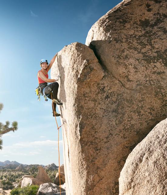 A woman climbing a rocky cliff in the desert on a sunny afternoon. Captured as part of the "Let's Play" production.